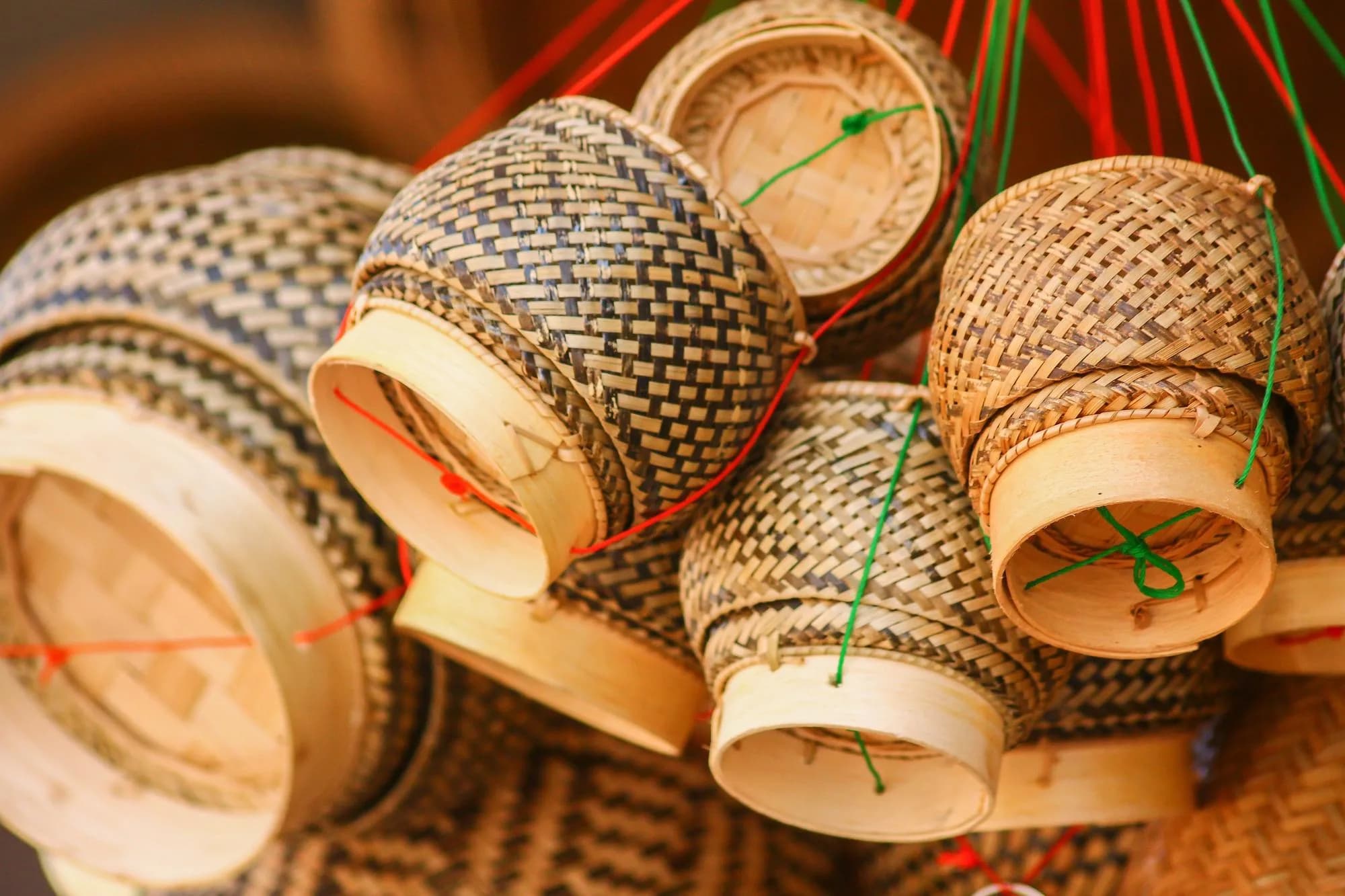 Handwoven bamboo baskets with geometric patterns hanging by colorful cord