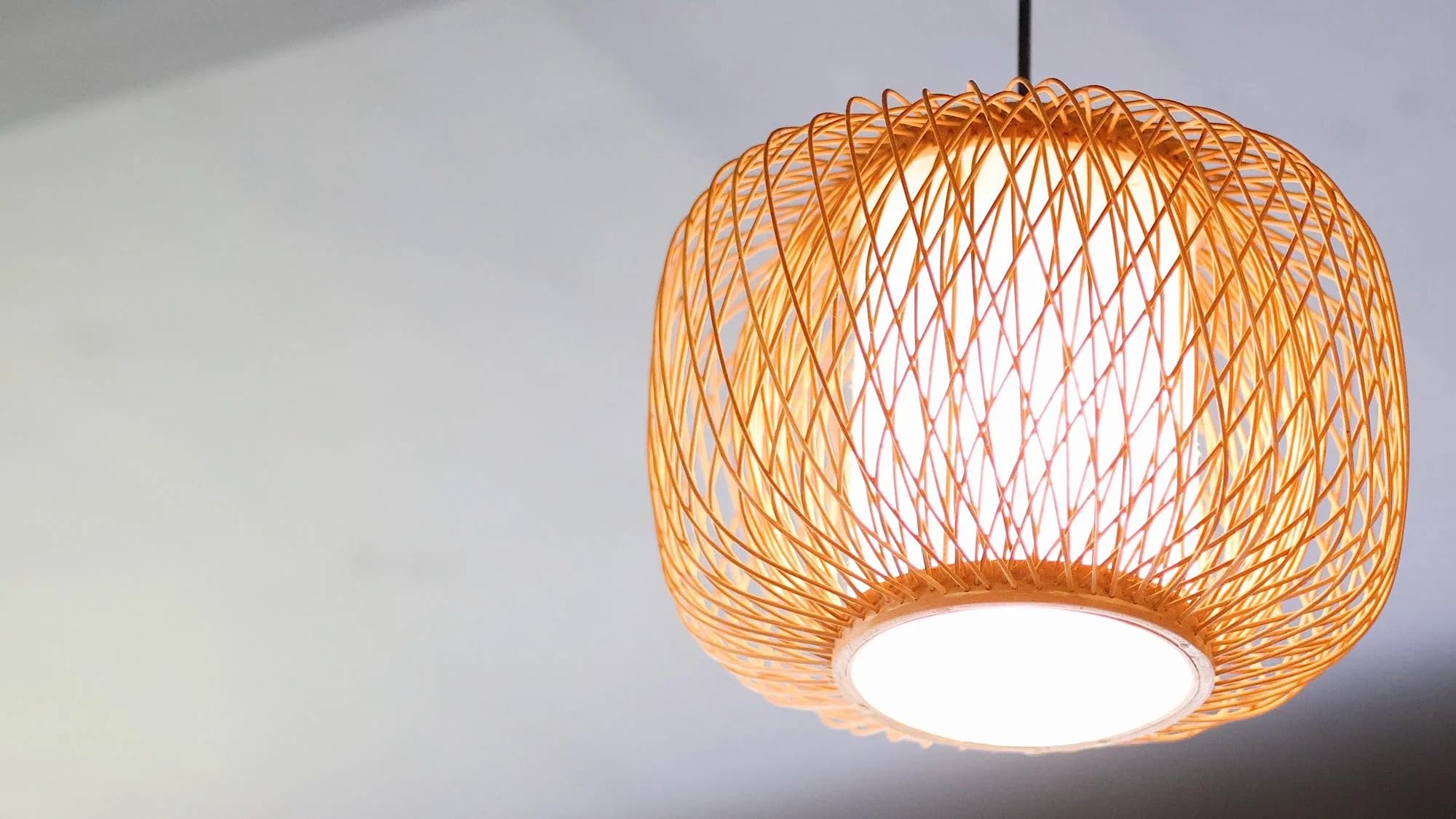 Woven bamboo pendant lamp glowing against a soft neutral wall